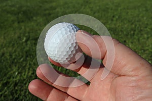 Close-up of a hand holding a golf ball. Green blurred background.