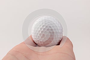 Female hand holding golf ball on light background. The white color of plastic ball is popular in the game