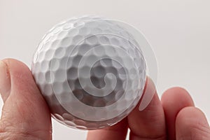 Female hand holding golf ball on light background. The white color of plastic ball is popular in the game