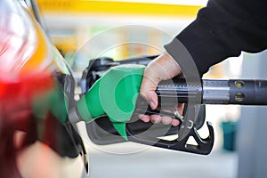 Close up hand holding green gasoline fuel nozzle and being fill gas tank of black car in gas station Concept of Global Fossil Fuel