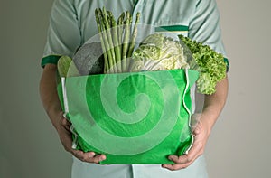 close up hand holding green grocery bag of mixed the organic green vegetables , healthy organic green food shopping and diet heal