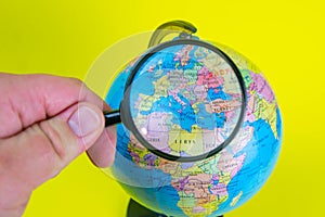 Close-up of a hand holding a magnifying glass to look at the globe in the library selective focus Europe