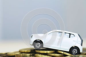 Close up hand holding model of toy car white on over a lot money of stacked coins