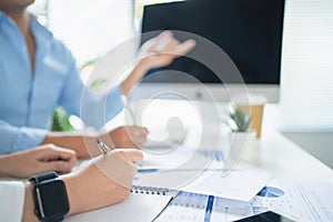 Close-up of a hand holding a pen. Asian business people are exchanging ideas about charts and graphs that show the results of