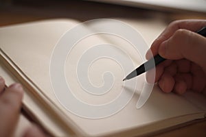 Close up of hand holding pen and writing on empty book paper, selective focus