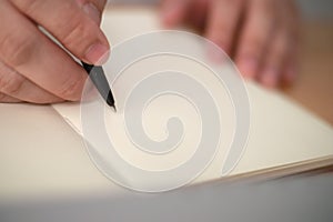 Close up of hand holding pen and writing on empty book paper, selective focus