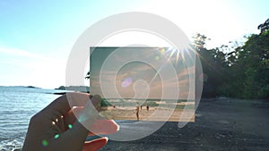 Close up hand holding photograph in front of beautiful tropical beach travel concept. Sun shining beautiful day