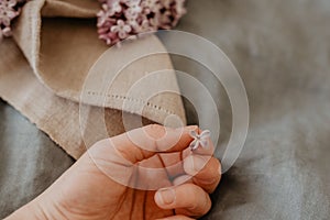 Close-up of hand holding purple lilac flowers with branch in bloom on blue linen sheet with neutral linen towel in the background