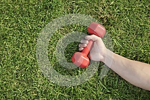 Close up on hand holding red dumbbell in grass, view from above