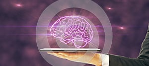 Close up of hand holding tablet with glowing human brain on dark purple background.