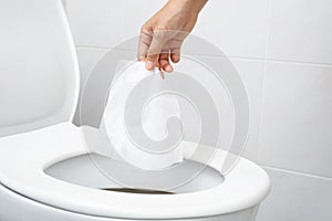 close up hand holding a tissue to be thrown into the toilet bowl. Can not drain water of toilet paper