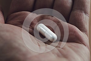 close up of a hand holding a white capsule pill