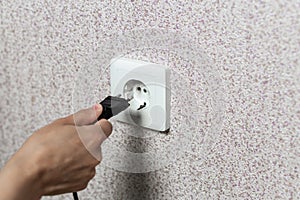 Close-up of a hand inserting a black plug into a white socket