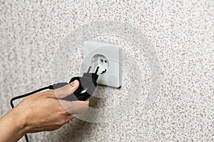 Close-up of a hand inserting a black plug into a white socket.