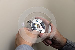 Close-up of Hand installing mounting plate for modern round thermostat for air conditioning unit