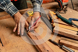 Close-up hand of male carpenter using pencil on a piece of wood on construction site