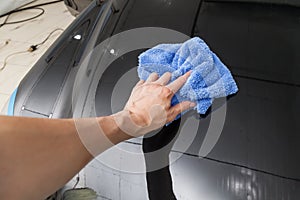 Close-up on the hand of a male cleaner with a blue microfiber cloth that wipes a black car after washing and applying a protective