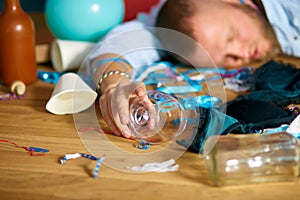 Close up of hand man hold a glass of brandy, sleeping at table in messy room after bachelor party