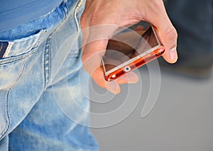 close up of the hand of a man holding his phone between his finger. The man ÃÂ´s hand is at his back. He is no using his mobile