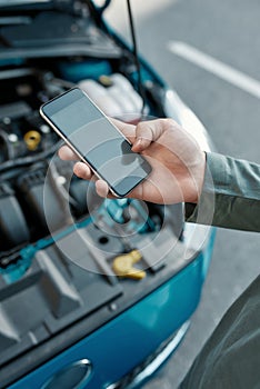 Close up of hand of man holding phone, calling emergency car service while standing near his broken car with open hood