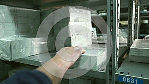 Close up hand of Man takes box from shelf inside warehouse