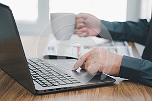 Close up hand a man touch on mouse pad of laptop and hold coffee cup