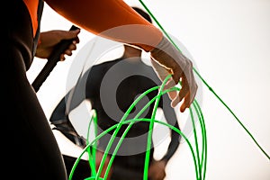 Close-up of hand of man in wetsuit holding bright green rope.