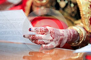 Close up of hand and nails of Asian Muslim bride with henna tattoo and jewelry holding paper contains prayer in wedding ceremony