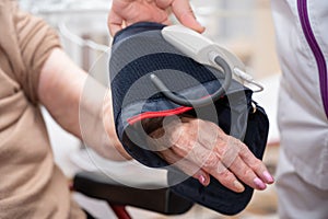 Close up hand of nurse working and adjusting blood pressure gauge on senior woman hand in nursing home