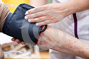 Close up hand of nurse working and adjusting blood pressure gauge on senior woman hand in nursing home