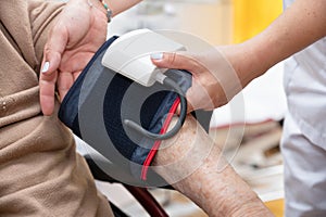 Close up hand of nurse working and adjusting blood pressure gauge on senior woman hand in nursing home