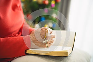 Close up hand. old senior woman doing hands together and holding necklace of crosses prayer to God along with the bible In the