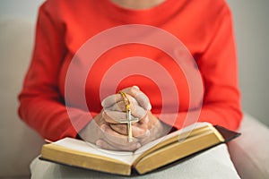 Close up hand. old senior woman doing hands together and holding necklace of crosses prayer to God along with the bible In the