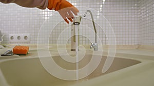 Close-up. A hand in an orange rubber glove first opens the water with a faucet in the kitchen sink, and then closes it.