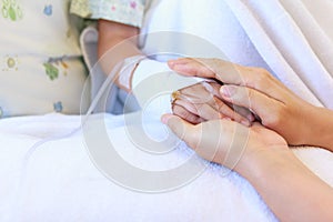 Close up hand of parent holding hand of child in hospital.