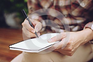 Close up hand people man are sitting on a chair wooden. using pen writing Record Lecture note pad into the book in park public.