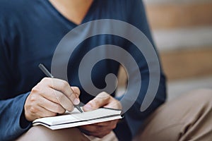 Close up hand people man are sitting on a staircase. using pen writing Record Lecture note pad into the book in park public.