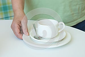 Close-up of a hand picking up a stack of plates and a dirty coffee cup from the table