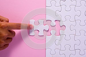 Close up of hand placing the last jigsaw puzzle piece on pink ba