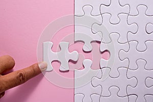 Close up of hand placing the last jigsaw puzzle piece on pink ba