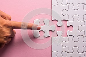 Close up of hand placing the last jigsaw puzzle piece on pink ba