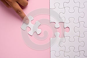 Close up of hand placing the last jigsaw puzzle piece on pink ba