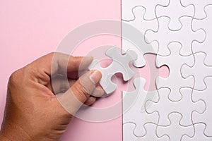 Close up of hand placing the last jigsaw puzzle piece on pink ba