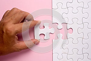 Close up of hand placing the last jigsaw puzzle piece on pink ba