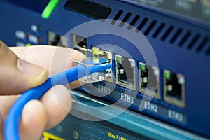 Close-up of a hand plugging a blue ethernet cable into a network switch or router. Concept data connection, internet technology,