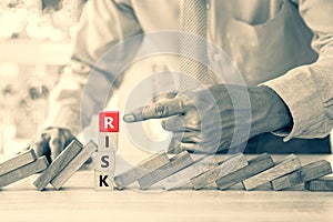 Close-up hand pointing risk text on wooden block stack with falling domino concepts of financial risk management and strategic