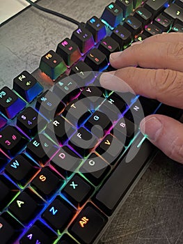 close up of a hand pressing the keys of a gaming computer keyboard, with backlit black keys changing color,human hand tapping a