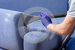 Close-up of a hand in a protective glove, cleaning the blue sofa from dirt