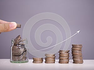 Close up hand putting coin into glass bottle, stack of coins with arrow rising. The concept of business growth, Financial