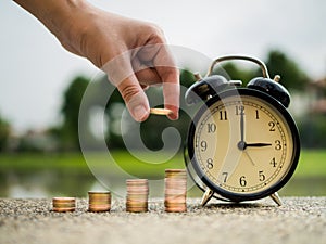 Close up hand putting money to stack of coins with time, time value of money concept in business finance theme. Saving money for f